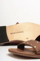 Sandalias bajas de cuero negro con tachas plateadas, tiras cruzadas y hebilla al tobillo.