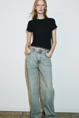 Camiseta de manga corta color marrón oscuro con textura acanalada, cuello redondo y bajo recto. Presenta un bajo superpuesto de tul o tela más clara, visible en el ruedo y en el cuello.