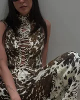 Conjunto de dos piezas con estampado de vaca en tonos marrón y blanco. Incluye un top sin mangas con cuello alto y cierre frontal mediante cordones cruzados, y un pantalón de corte holgado a juego.