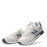 Championes urbanos New Balance modelo 574, con diseño híbrido en tonos beige y detalles en azul marino. Confeccionados en una combinación de gamuza y malla, cuentan con tecnología de amortiguación ENCAP en la entresuela para mayor estabilidad y soporte.