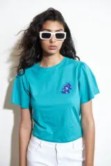 Remera turquesa de algodón con cuello redondo y mangas cortas abullonadas. Presenta un bordado en el pecho con forma de animal.