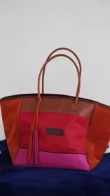 Bolso de fin de semana estilo tote de lona con estampado camuflado, detalles en cuero marrón y gamuza azul, manijas largas y borla decorativa colgante.
