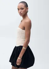 Vestido corto de diseño combinado con cuerpo strapless drapeado en color beige y falda estilo globo en color negro. Cuenta con cierre lateral invisible.