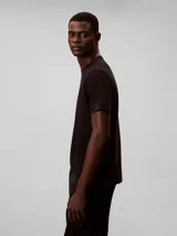 Remera de algodón negro con cuello redondo y manga corta. Presenta un estampado gráfico en el pecho con el monograma de Calvin Klein en colores azul, verde y rojo, junto con el nombre de la marca debajo.