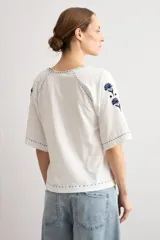 Remera blanca de manga corta con escote en V, decorada con delicados bordados florales en azul oscuro en el pecho, hombros y mangas.