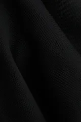 Top largo de punto tupido, color negro, con hombros descubiertos, corte ajustado y diseño acampanado estilo peplum desde la cintura.