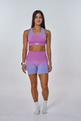 Conjunto deportivo compuesto por un top y un short de ciclismo, ambos con diseño degradado que transiciona de fucsia a lila. El top presenta cuello redondo y logo 'bk.' estampado en el frente, mientras que el short es de tiro alto y ajuste ceñido.
