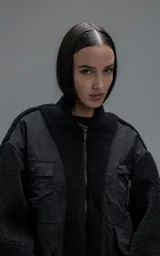 Campera estilo bomber unisex, confeccionada en una combinación de corderito sintético y paneles de ripstop. Presenta un diseño utilitario con múltiples bolsillos frontales con cierres y broches a presión, cuello, puños y ruedo en ribb elástico.