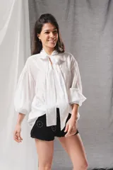 Blusa blanca holgada con mangas abullonadas y lazo en el cuello para anudar.