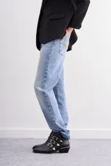 Bota de caña corta confeccionada en cuero vacuno negro. Presenta tres tiras decorativas con remaches metálicos y hebillas sobre la capellada, puntera metálica, cierre lateral interno y taco ancho con detalle de vira metálica.