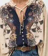 Blusa tipo bata de viscosa con estampa floral estilo paisley. Presenta cuello alto con detalle de volados, cierre frontal con botones y lazo ajustable en el escote. Posee mangas largas abullonadas con puños elásticos.
