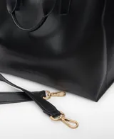 Bolso shopper horizontal negro de piel sintética, con dos compartimentos, cierre magnético y bolsillo interior con cremallera. Cuenta con asa de mano y correa larga regulable y extraíble, además del logo grabado en el frente.