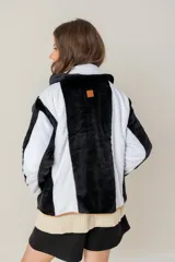 Campera de textura suave y afelpada con diseño de rayas verticales en blanco y negro. Presenta un corte recto, cuello con solapas y cierre frontal con botones. Los bordes están terminados con un ribete en color tostado que aporta contraste y estructura a la prenda.