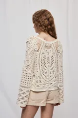 Sweater corto color crudo de manga larga, confeccionado en crochet calado con diseño artesanal y silueta amplia.