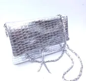 Cartera plateada tipo bandolera con solapa y cierre magnético. Tiene una cadena corta y una cadena larga.