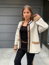 Chaqueta color crema con ribetes en marrón y negro, de lana merino, con cuello redondo, cierre frontal con botones y bolsillos de parche.