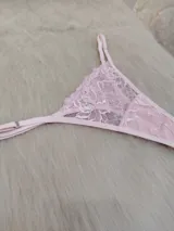 Microtanga de encaje rosado con diseño de tiras laterales regulables y detalle de aplique brillante en el centro.
