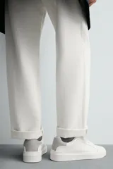 Zapatilla deportiva de cuero sintético color blanco, con suela de plataforma gruesa y detalle de gamuza gris en el talón.