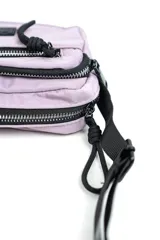 Bandolera de nylon color lila con múltiples compartimentos con cierre, tira ajustable negra y detalle de etiqueta engomada en el frente.