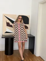 Vestido corto tejido en jacquard de algodón a cuadros marrones y beige, con terminaciones en color rosa. Tiene cuello redondo, botones frontales y corte sin mangas.