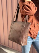 Cartera shopper de cuero color marrón chocolate, con doble asa de hombro, bolsillo frontal externo y diseño estructurado.