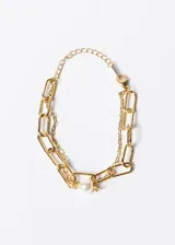 Pulsera dorada con doble cadena, una de eslabones rectangulares grandes y otra de eslabones finos. Tiene un dije de perla blanca.