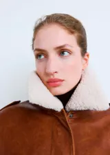 Chaqueta estilo aviador de cuero sintético en color marrón, con cuello y solapas de corderito sintético en color blanco. Presenta cierre frontal de cremallera, bolsillos frontales con solapa, puños y dobladillo de canalé elástico.