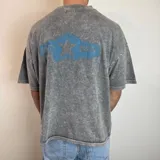 Remera de corte boxy con efecto lavado ácido en color gris. Presenta un estampado gráfico en la espalda con una franja azul horizontal, una estrella central y la inscripción 'WHITE NOISE'.