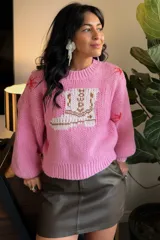 Suéter de punto color rosado con diseño frontal de bota vaquera y detalles de estrellas pequeñas en color rojo. Presenta cuello redondo, mangas largas tipo balón y puños acanalados.