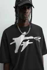 Camiseta negra de corte relaxed fit, cuello redondo y manga corta. Presenta un estampado frontal en blanco con efecto spray que simula dos figuras volando, y texto en un óvalo que dice "SUCCESS CHASER".