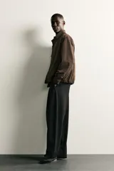 Pantalón de corte balloon fit en color gris oscuro, confeccionado en tejido con viscosa. Presenta pliegues frontales, cintura ajustable con cinturón integrado, bolsillos laterales y bolsillos traseros de doble vivo. Cierre frontal con cremallera y botón.