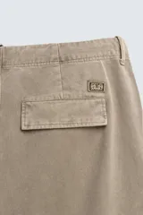 Pantalón cargo de corte relajado con efecto lavado, confeccionado en tejido de algodón. Presenta bolsillos frontales, bolsillos traseros con solapa y bolsillos con cierre de cremallera en las perneras. Incluye pliegues en las rodillas y ajuste en los tobillos.