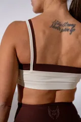 Top deportivo de doble capa en color crema con detalles en marrón oscuro, con breteles finos y logo bordado en el centro del pecho.