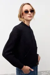 Cardigan negro de tejido de punto con sutiles destellos brillantes, cuello redondo, cierre frontal con botones y mangas largas con puños acanalados.
