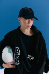 Gorra tipo cap confeccionada en corderoy negro, con isologo bordado en el frente y tira de ajuste con hebilla metálica en la parte posterior.