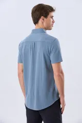 Camisa de piqué lisa color celeste, de manga corta, con cuello camisero y cierre frontal de botones oscuros.
