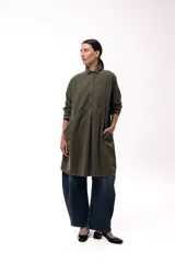 Vestido camisero de silueta amplia y fluida, color verde militar, con cuello camisero, frente abotonado parcial, mangas largas y bolsillos laterales.