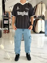 Camiseta deportiva blanca de manga corta con rayas verticales negras, cuello polo en V de color negro con ribete blanco, y puños negros. Cuenta con estampado frontal con la palabra "TOKIO" en grande, además de detalles gráficos y texto en el pecho.