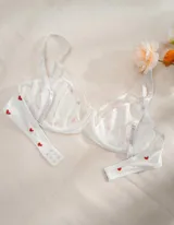 Soutien blanco con estampado de corazones rojos, con breteles finos regulables y moño decorativo en el centro.