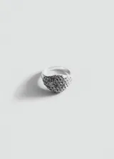 Anillo de metal plateado con diseño de sello redondeado, cubierto completamente por pequeños cristales brillantes.