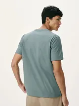 Camiseta blanca de algodón con cuello redondo y mangas cortas. Estampa rectangular con borde negro que contiene la frase "NATURAL ATMOSPHERE" en letras mayúsculas y una imagen de montañas y mar.