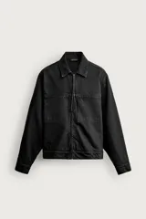Sobrecamisa de denim de algodón en color negro con efecto lavado, corte regular fit, cuello solapa y cierre frontal de cremallera. Presenta bolsillos de plastrón en el pecho y mangas largas con puños abotonados.