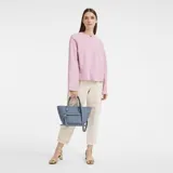 Cartera de cuero tipo tote con asas cortas y correa larga desmontable. Presenta un diseño estructurado con un bolsillo frontal con solapa y detalle de logo metálico.