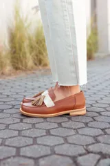 Mocasines de cuero color tostado, con detalle de antifaz en cuero crudo y borlas decorativas. Hechos a mano en Uruguay.