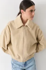 Campera bomber de paño color beige, con cierre frontal, cuello alto y puños elásticos.