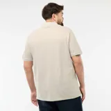 Remera tipo polo de manga corta en color beige, con cuello clásico y detalles de ribete en contraste en el borde del cuello y las mangas. Presenta cierre frontal con tres botones y un pequeño logo bordado en el pecho.