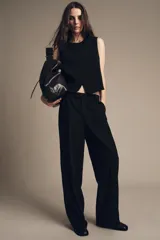 Chaleco negro de cuello redondo y sin mangas, con cierre frontal cruzado con un botón y bajo asimétrico.