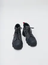 Bota acordonada de estilo montañés con suela track de goma robusta. Confeccionada en cuero con detalles de gamuza en la talonera y tirador trasero. Presenta costuras a contratono y cordones bicolores.