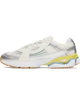 Championes deportivos UA Sola con diseño retro-futurista. Presentan una combinación de malla técnica y superposiciones sintéticas en tonos crema, con detalles en plateado metalizado, amarillo vibrante y azul claro. Incluyen entresuela de EVA acolchada y suela de goma color caramelo.