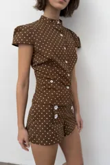 Shorts mini de tiro medio con estampado de lunares blancos sobre fondo marrón. Presenta cierre frontal decorado con botones blancos y bolsillos laterales.